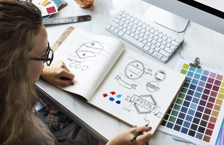 Diseñadora bocetando un logotipo junto a una carta de colores