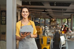 Dependienta con delantal consultando una tableta en un local comercial