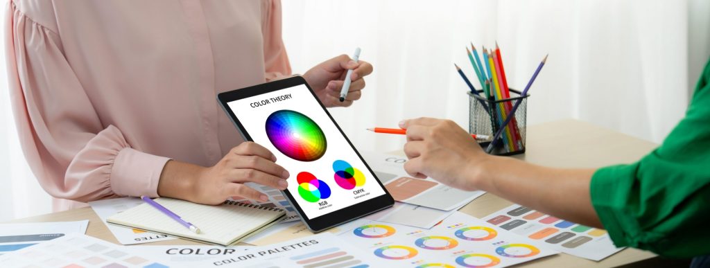 Dissenyadora seleccionant colors en una tauleta al costat de mostres impreses