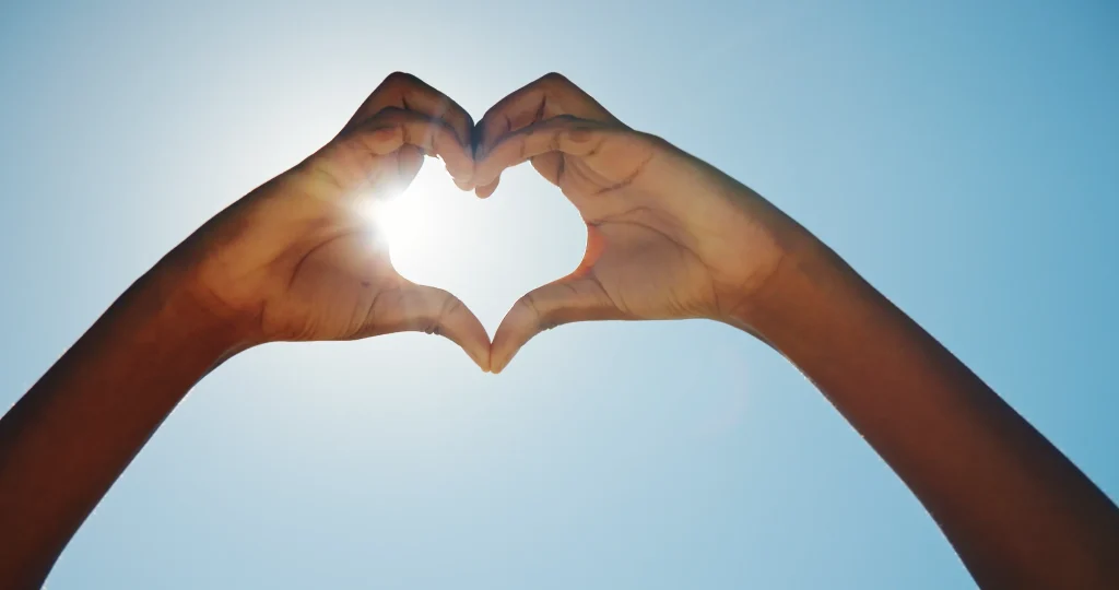 Manos formando un corazón a contraluz sobre el cielo