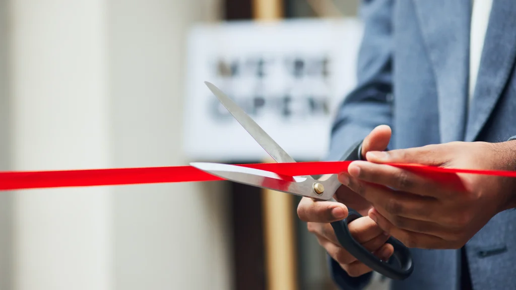 Corte de cinta inaugural con un cartel de we're open al fondo